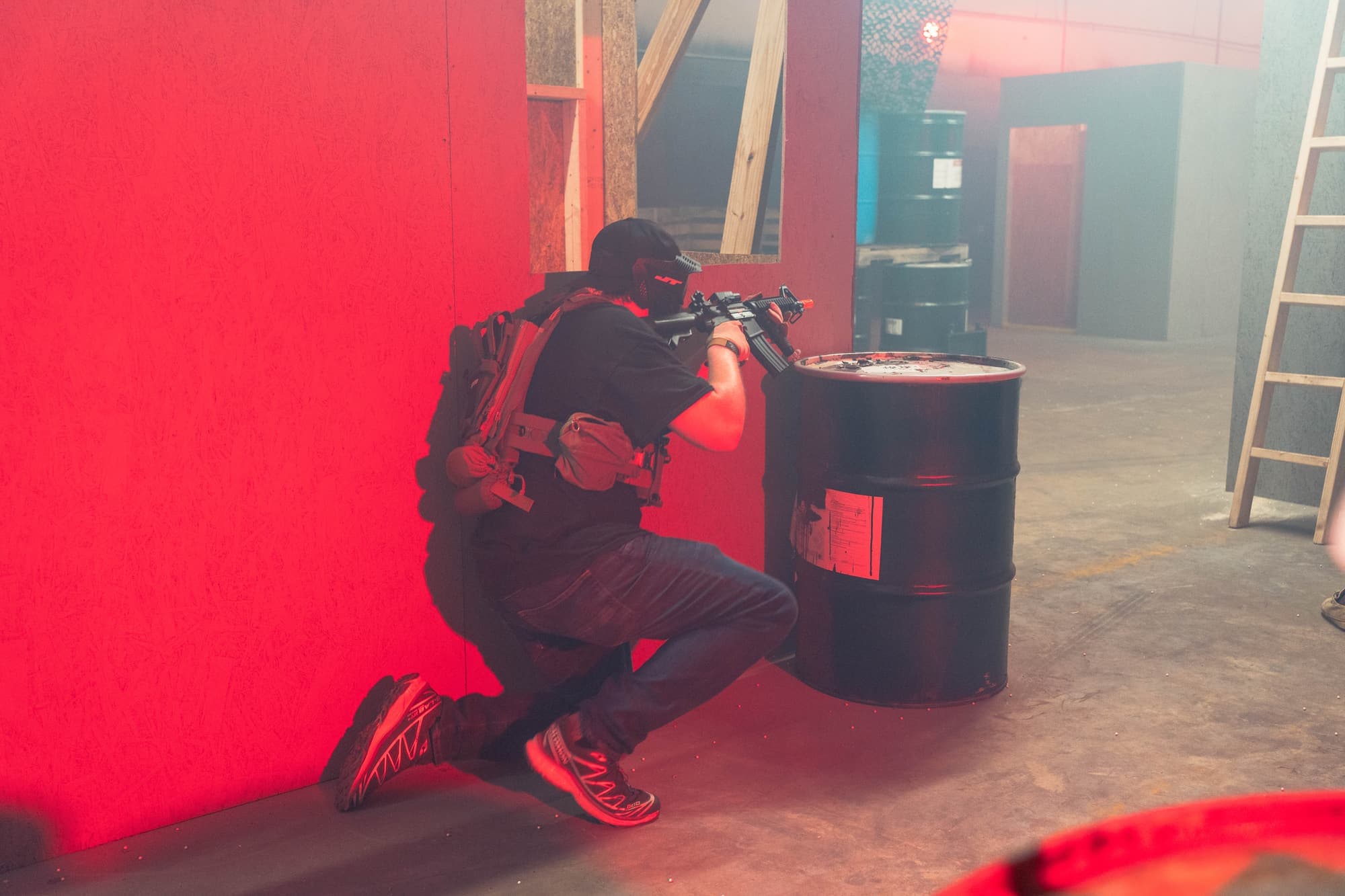 Player in a mask kneeling behind a barrel under red arena lighting